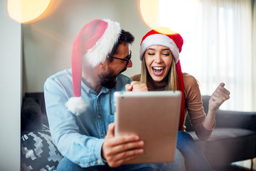  Love couple with Christmas hats on head using tablet and smiling