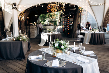 Wedding banquet. Round tables which are beautifully decorated with plates, candles and a beautiful composition of flowers