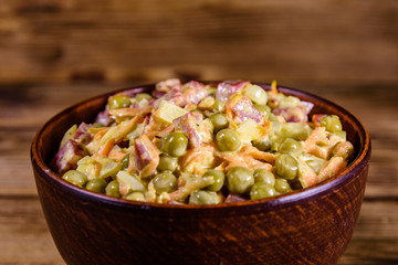 Salad with sausage, green pea, onion and carrot in glass bowl on wooden table