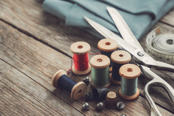 Retro sewing items: tailoring scissors, thimbles, buttons, wooden thread spools, measuring tape and green fabric.