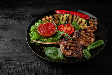 Rack of lamb calf with grilled vegetables, herbs and spicy tomato sauce. Nutritious, dietary, fitness food. Black boards background