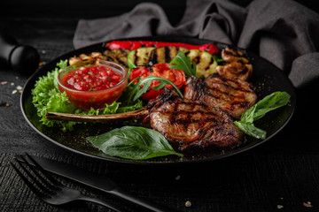 Rack of lamb calf with grilled vegetables, herbs and spicy tomato sauce. Nutritious, dietary, fitness food. Black boards background