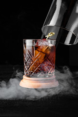 Manhattan cocktail whiskey with ice in smoke. Restaurant menu on a black background. Cocktail card.