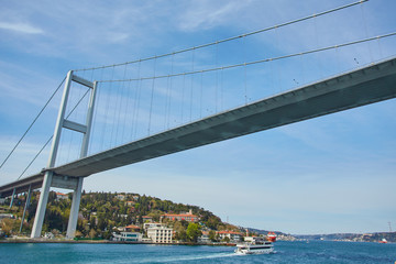 Ships passing through Bosphorus Bridge with background of Bosphorus strait on a sunny day with background cloudy blue sky and blue sea in Istanbul, Turkey.