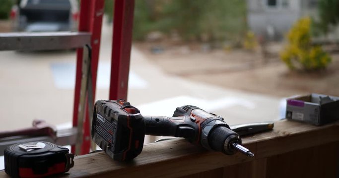 A male construction worker hauling building materials on the job site with power tools and equipment on the incomplete home framing.
