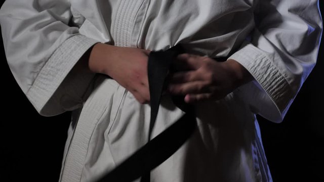 Close-up front view of a Karate Judo fighter's waist as they tie on a black belt.