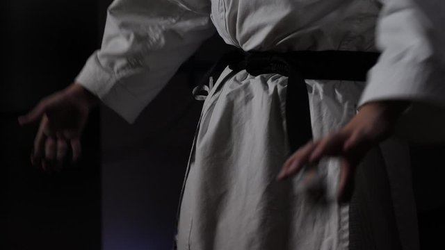 Close-up of a Karate Judo fighter putting on and tightening a martial arts black belt over his Judogi. Three-quarters view with copy space.