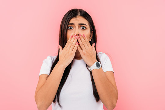 scared pretty brunette girl covering mouth with hands isolated on pink