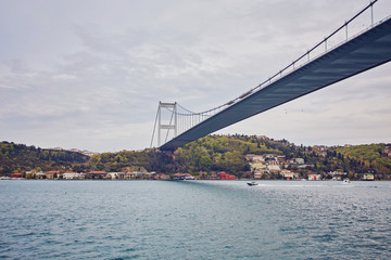 Ships passing through Bosphorus Bridge with background of Bosphorus strait on a sunny day with background cloudy blue sky and blue sea in Istanbul, Turkey.