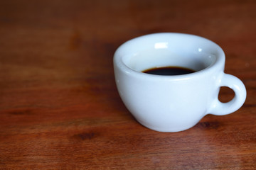 A white old cup for espresso stands with coffee on a wooden table