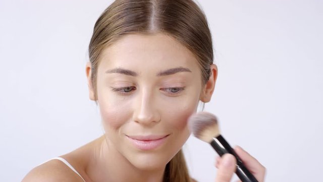 Close up shot of beautiful young woman smiling and applying blush on cheekbone