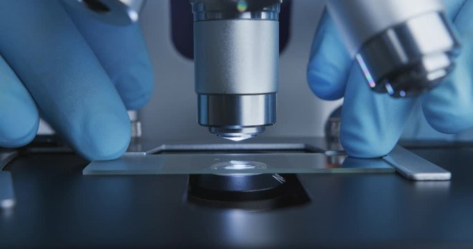 Close-up shot of sample slide and microscope with metal lens at laboratory.