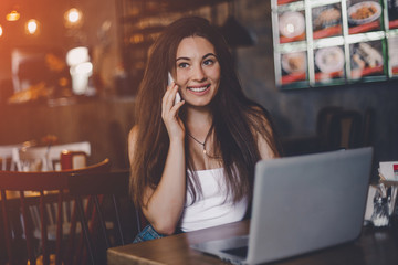 Business woman talking to the phone, working on a laptop and drinking coffee in a cafe.