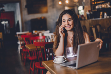 Business woman talking to the phone, working on a laptop and drinking coffee in a cafe.