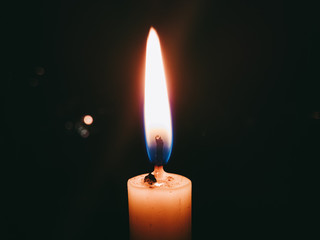 Flame from lighted wax candle with a calm fire beam on dark background