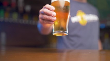 Slow motion of bartender in a pub placing a full pint of beer on bar in front of camera.