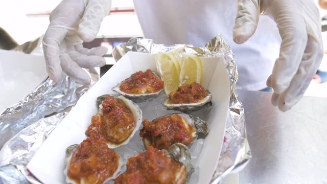 Two slices of lemon are placed on a serving of oysters with tomato sauce before the plate is pushed toward the camera in an inviting manner.