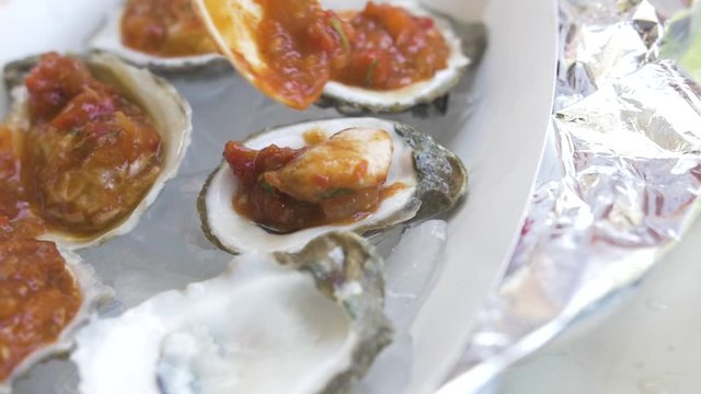 An oyster covered in spicy tomato sauce is placed back onto its shell in a beautiful delicious serving.