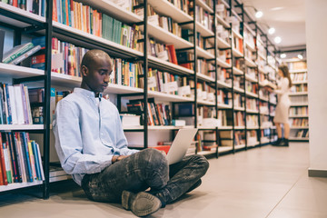 Ethnic man browsing laptop in library