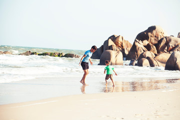 happy family on beach playing, father with son walking sea coast, rocks behind smiling taking vacation