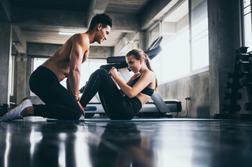 Personal trainer helping woman exercising in the sport gym - obrazy, fototapety, plakaty