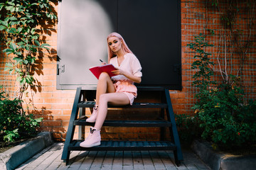 Attentive modern woman writing in red notebook on metal stair