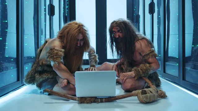 Wild savages using laptop computer in digital server room. Primitive cavemen running diagnostics in database working with new technology. Time travellers.