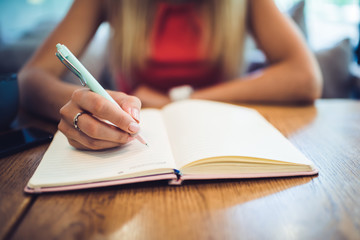 Crop woman writing in diary in cafe