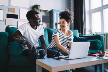 Multiracial couple looking at each other with smile sitting on sofa