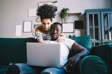 Shocked black couple browsing laptop on couch