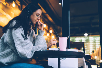 Thoughtful young woman in headphones surfing tablet in cafe