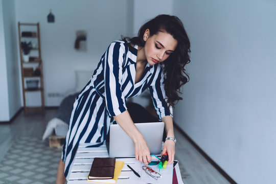 Engaged woman stooping over desk and turning over stationery