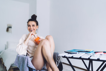 Pleased woman drinking beverage while sitting at desk at home