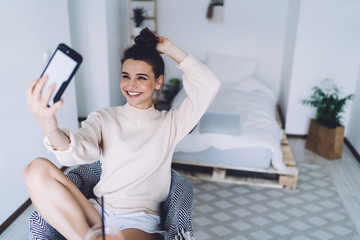 Happy woman taking selfie with smartphone in bedroom