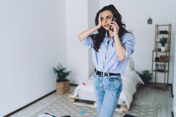 Young busy woman standing in bedroom and using smartphone