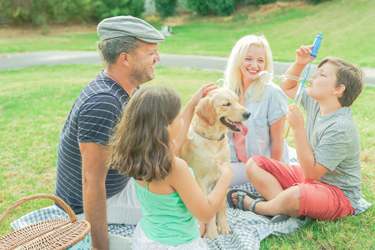 Happy family with their dog in a good sun day. The boy playing with soap bubbles. Happy family doing picnic in the park .  Image