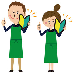 ポップな緑のエプロンをした紺の長袖の男女が初心者マークを持つ