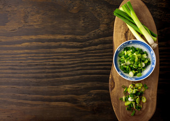 Chopped spring onion, scallion on wood board and wood background.