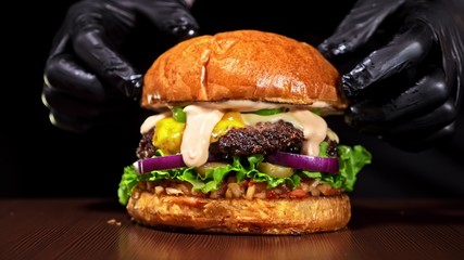 Craft burger is cooking on black background. Consist: red sauce salsa, lettuce, red onion, pickle,...