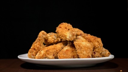 Cool beautiful fresh juicy cooked chicken wings in breading. Buffalo wings spread on food white plate in table. Very tasty and beautiful. Cooking with deep fryer fry machine.