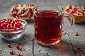 Glass mug with pomegranate juice and pomegranate seeds on a wooden table.