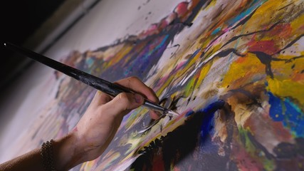 Artist designer draws an eagle on the wall. Craftsman decorator paints a picture with acrylic oil color brush. Close-up dark magic cinematic look. Painter dressed in a paint coat. Indoor.