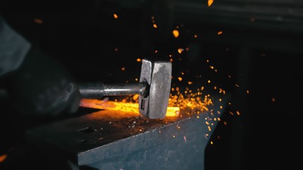 Forge workshop. Smithy manual production. Hands of smith with hammer hit on glowing hot metal, on...