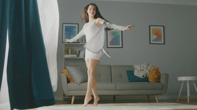 Beautiful Young Brunette Opens Curtains To let Morning Sunlight Illuminate Her Cozy Apartment, She Proceeds Dancing Beautifully and Quite Professionally across Room. Slow Motion Low Angle Side View
