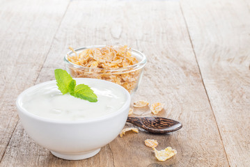 Yogurt in a white cup with a healthy breakfast cereal, placed on a wooden table
