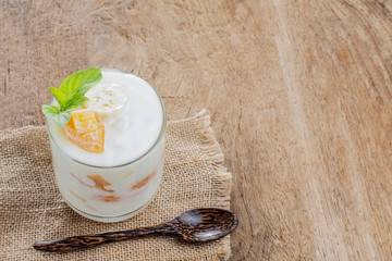 yogurt in a glass cup with oranges and bananas for a healthy breakfast laid on a wooden table.