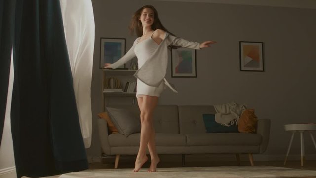 Beautiful Young Brunette Opens Curtains To let Morning Sunlight Illuminate Her Cozy Apartment, She Proceeds Dancing Beautifully and Quite Professionally across Room. Slow Motion Low Angle Side View