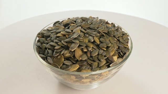 Nuts peeled pumpkin seed rotate are on a table in a plate. Snack in transparent dish on an isolated white background are spinning moving. Delicious and healthy protein-rich diet food.
