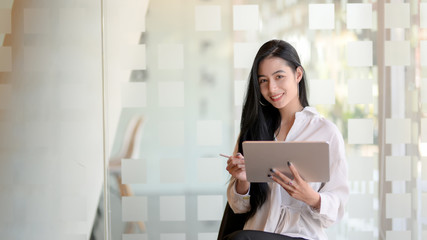 Portrait of young beautiful graphic designer working on her project with tablet and looking at the camera while standing in modern office