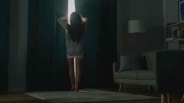Beautiful Young Brunette Opens Curtains To let Morning Sunlight Illuminate Her Cozy Apartment, She Proceeds Dancing Beautifully and Falling on the Couch, Fooling Around Happily. Following Back View